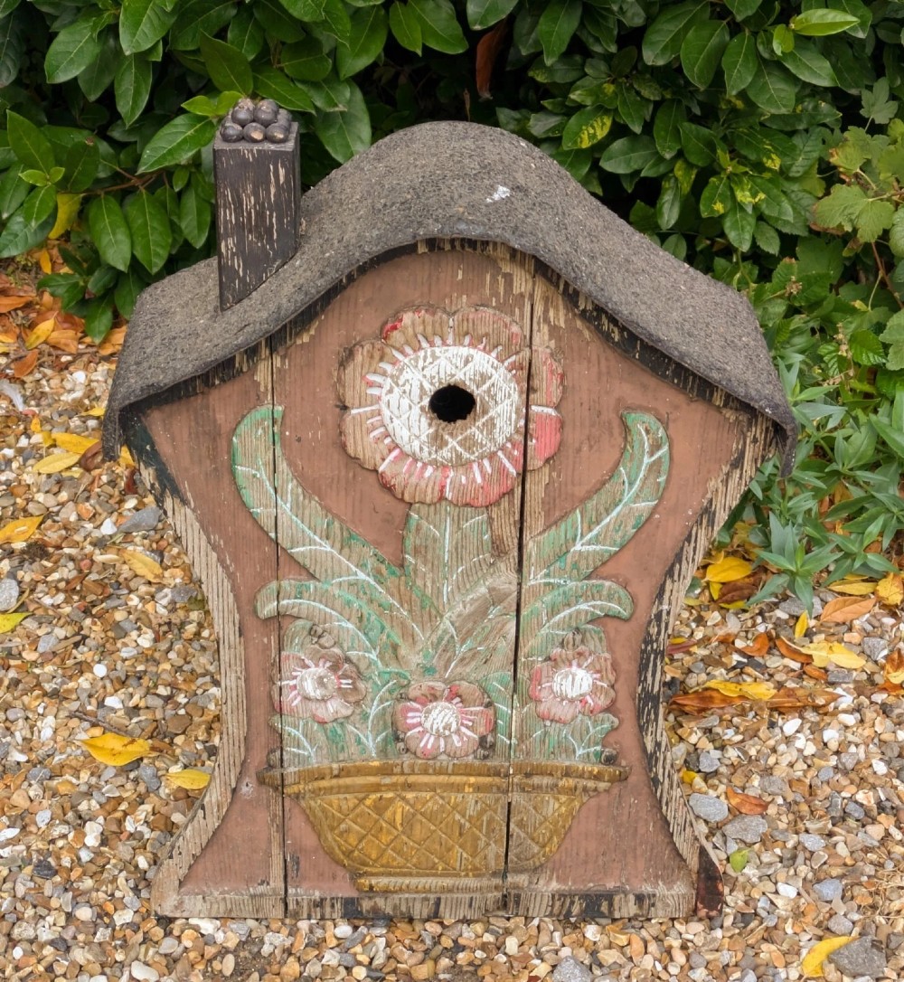 A carved and painted wooden Swedish birdhouse featuring a floral motif in a pot with a central entry hole and a chimney detail. View V