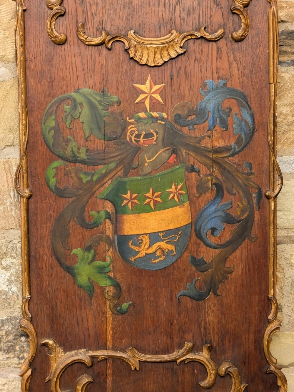 A rectangular carved oak wall plaque featuring a hand-painted heraldic coat of arms, gilt scroll moulding, and a Latin motto. View III
