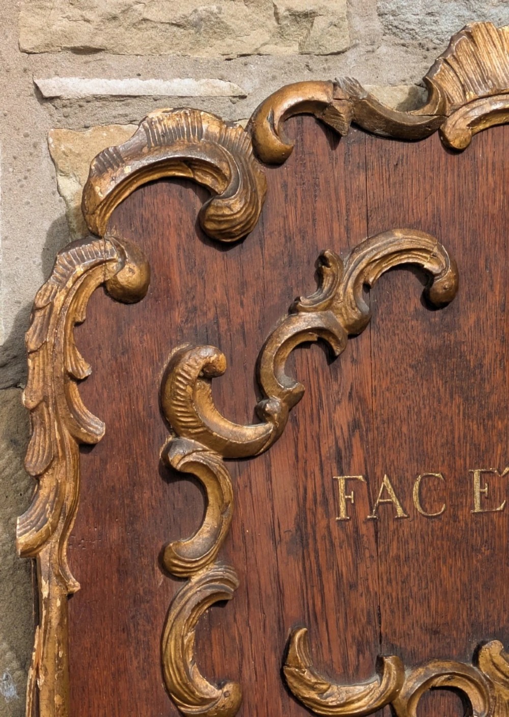 A rectangular carved oak wall plaque featuring a hand-painted heraldic coat of arms, gilt scroll moulding, and a Latin motto. View VI