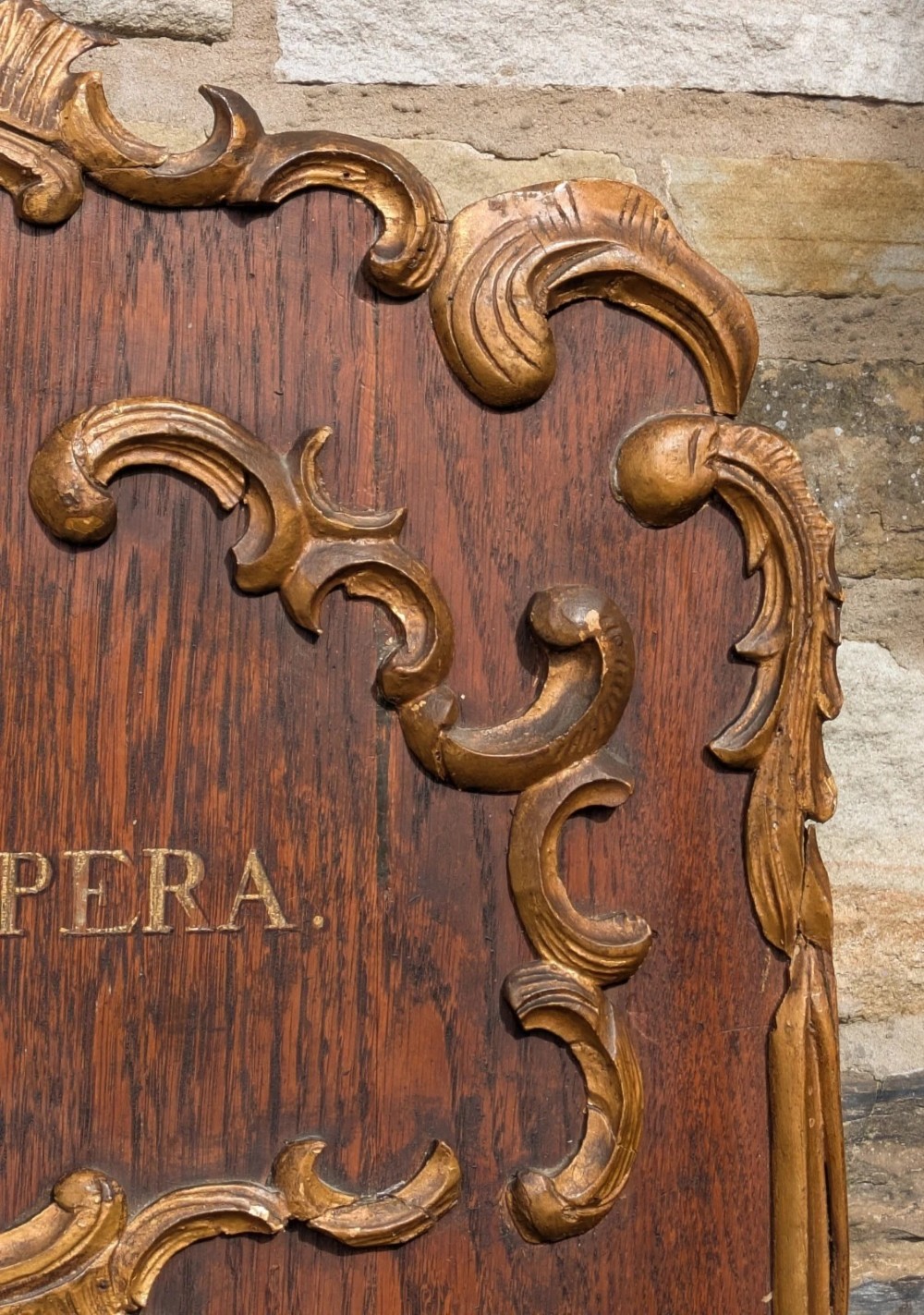 A rectangular carved oak wall plaque featuring a hand-painted heraldic coat of arms, gilt scroll moulding, and a Latin motto. View VII
