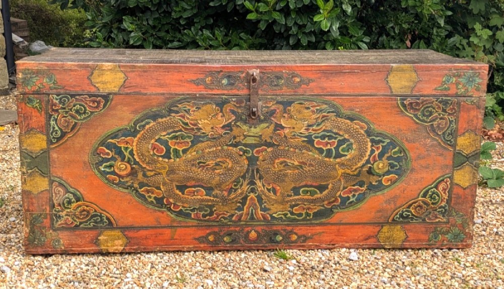 A rectangular wooden Tibetan storage chest decorated with hand-painted gold dragons on an orange ground with cloud borders and an iron latch.