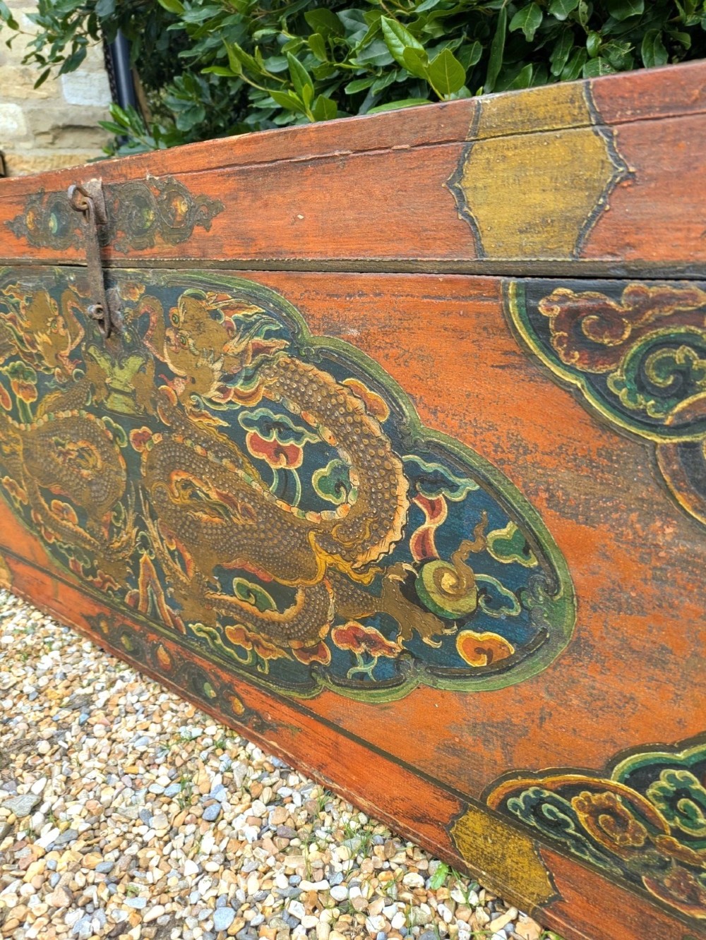A rectangular wooden Tibetan storage chest decorated with hand-painted gold dragons on an orange ground with cloud borders and an iron latch. View II