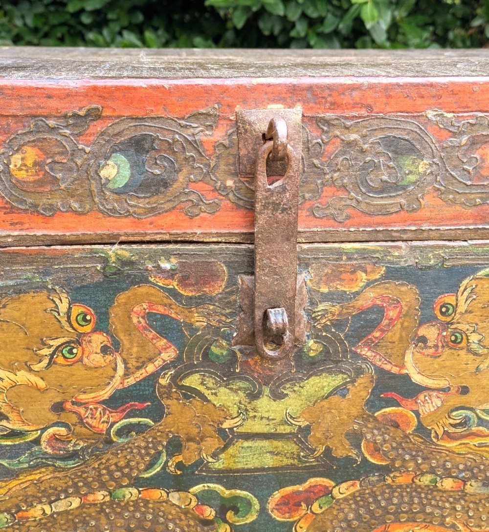 A rectangular wooden Tibetan storage chest decorated with hand-painted gold dragons on an orange ground with cloud borders and an iron latch. View IV