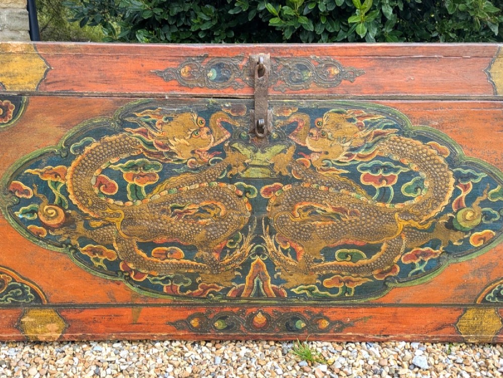 A rectangular wooden Tibetan storage chest decorated with hand-painted gold dragons on an orange ground with cloud borders and an iron latch. View V