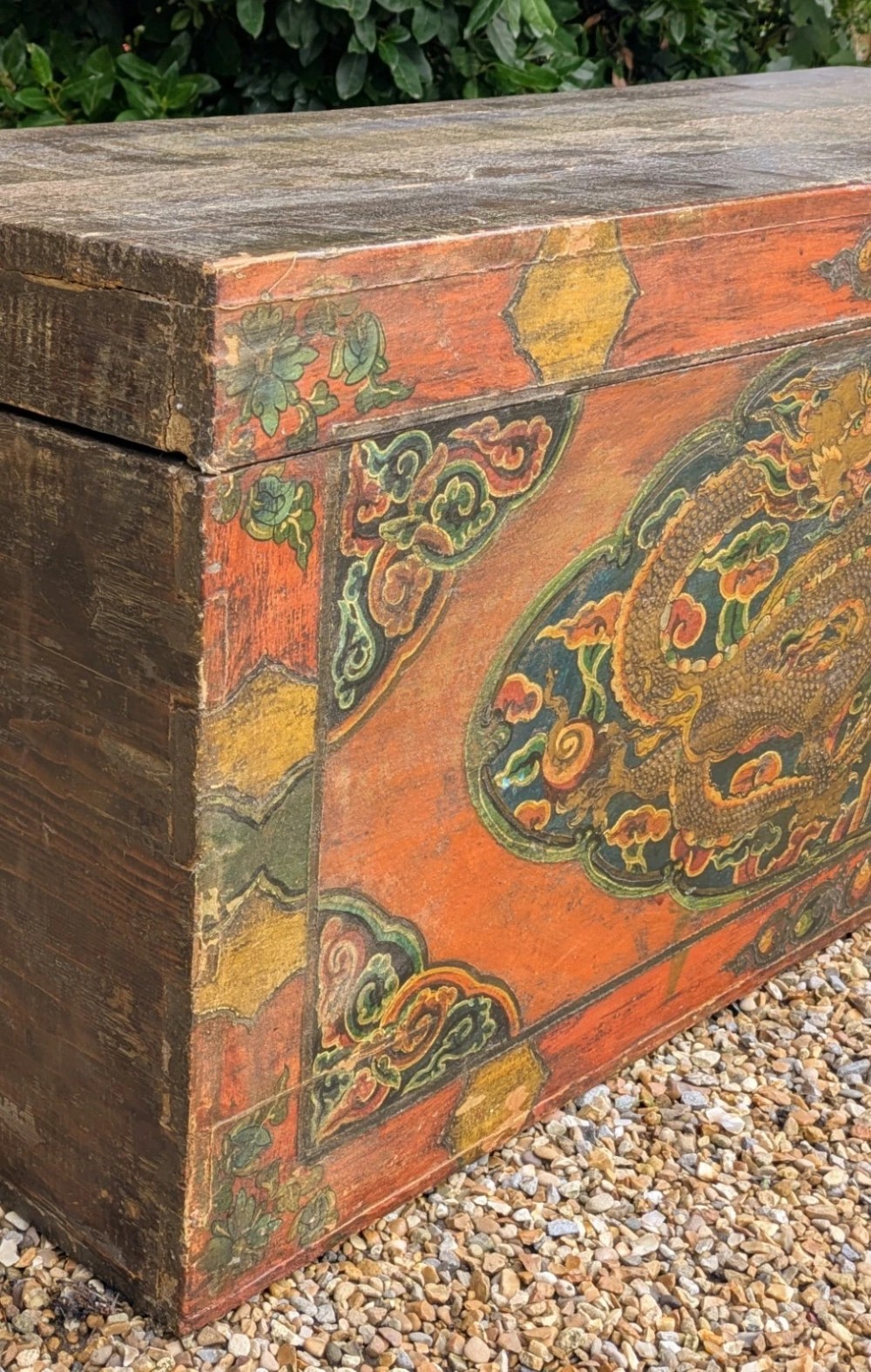 A rectangular wooden Tibetan storage chest decorated with hand-painted gold dragons on an orange ground with cloud borders and an iron latch. View VI