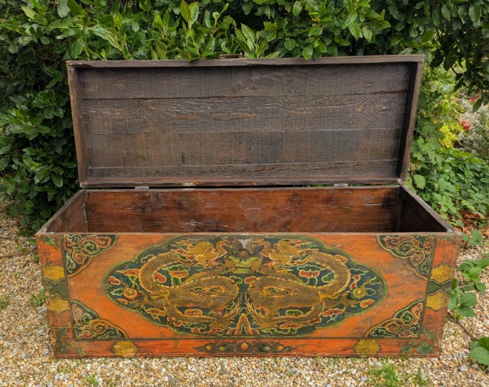 A rectangular wooden Tibetan storage chest decorated with hand-painted gold dragons on an orange ground with cloud borders and an iron latch. View VII