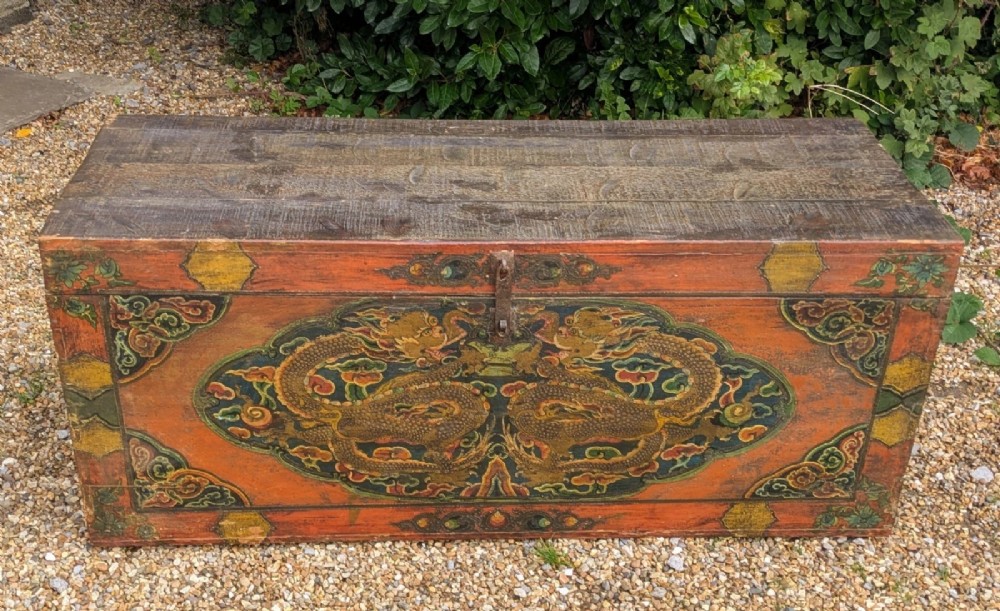 A rectangular wooden Tibetan storage chest decorated with hand-painted gold dragons on an orange ground with cloud borders and an iron latch. View VIII
