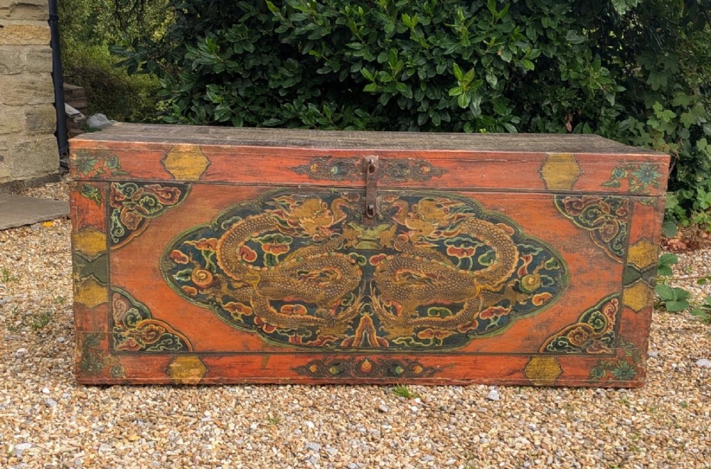 A rectangular wooden Tibetan storage chest decorated with hand-painted gold dragons on an orange ground with cloud borders and an iron latch. View X