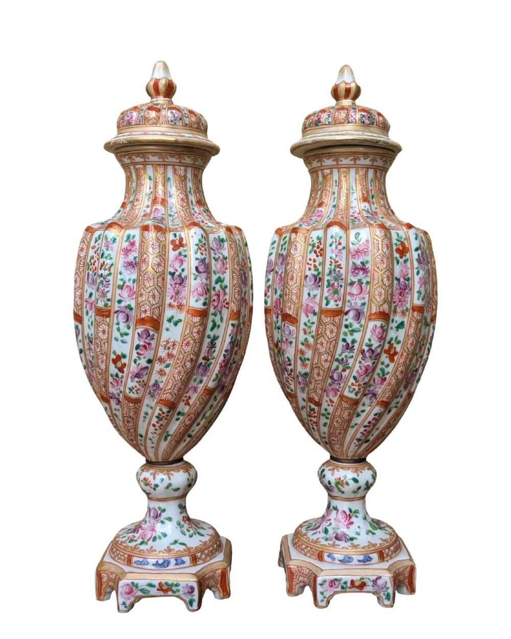 A pair of hand-painted porcelain lidded vases featuring fluted bodies, intricate floral motifs, geometric orange bands, and gilded details on square pedestals.