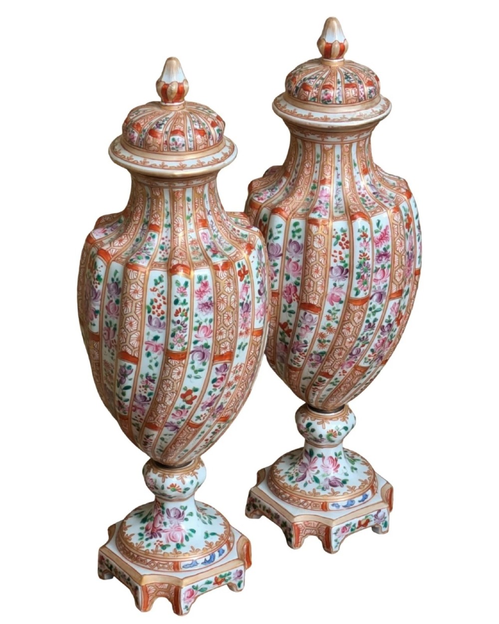 A pair of hand-painted porcelain lidded vases featuring fluted bodies, intricate floral motifs, geometric orange bands, and gilded details on square pedestals. View II