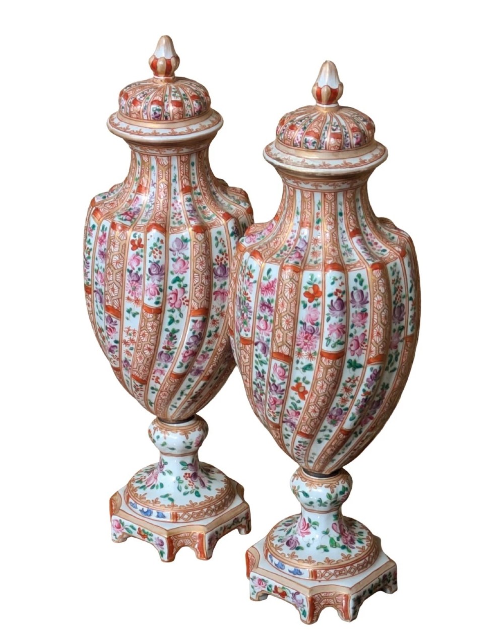 A pair of hand-painted porcelain lidded vases featuring fluted bodies, intricate floral motifs, geometric orange bands, and gilded details on square pedestals. View IV