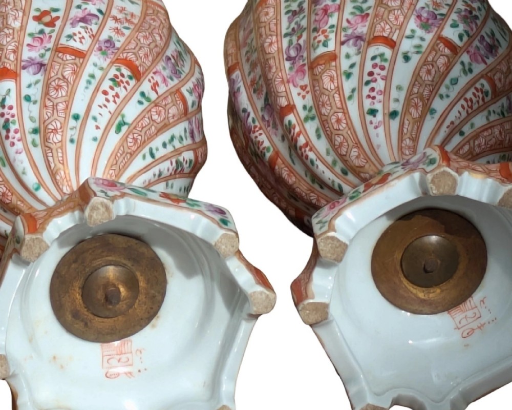 A pair of hand-painted porcelain lidded vases featuring fluted bodies, intricate floral motifs, geometric orange bands, and gilded details on square pedestals. View XII