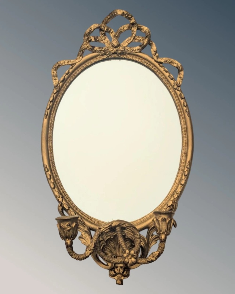 A matching pair of oval giltwood girandole wall mirrors featuring ribbon cresting and twin candle sconces at the base. View II