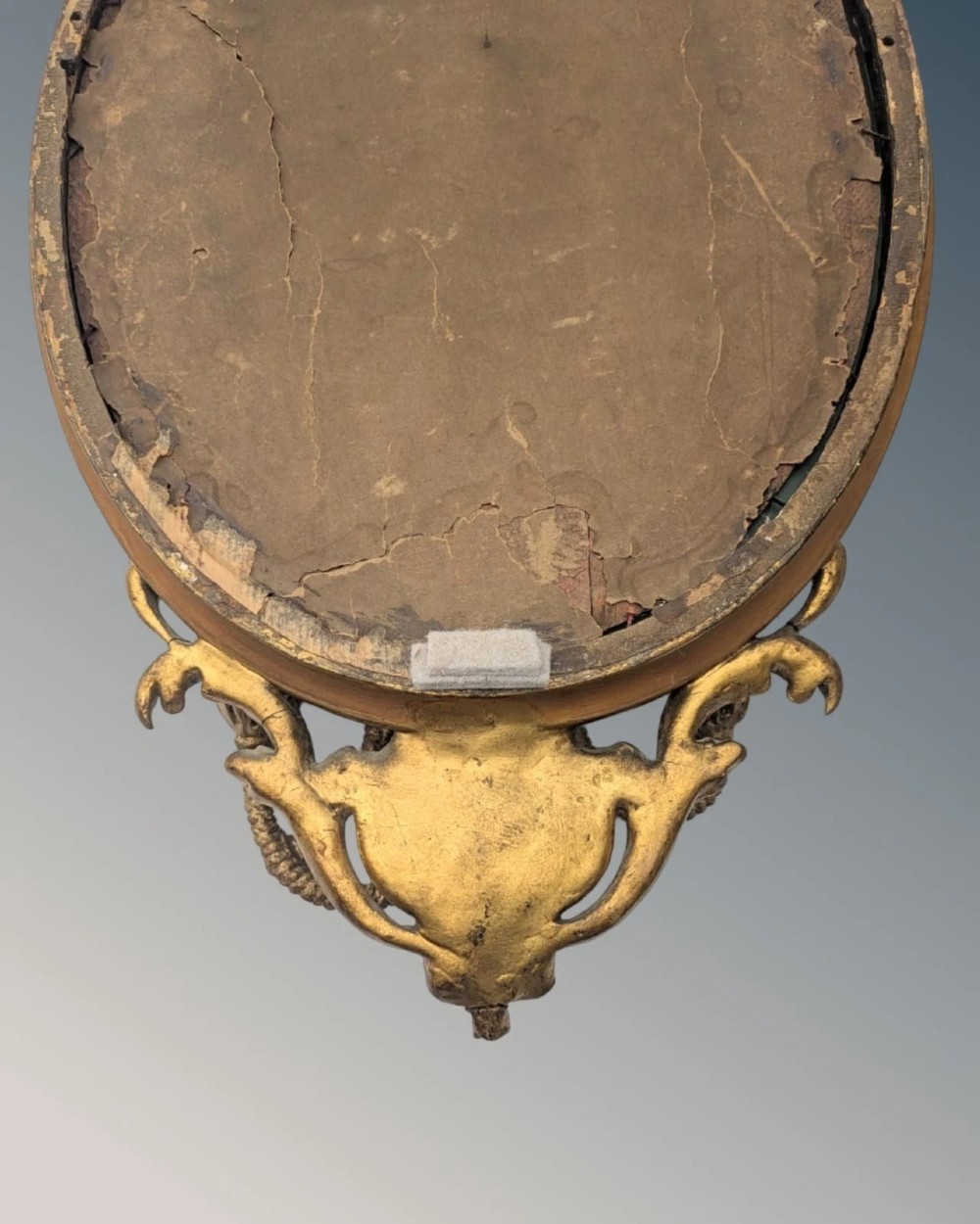 A matching pair of oval giltwood girandole wall mirrors featuring ribbon cresting and twin candle sconces at the base. View V