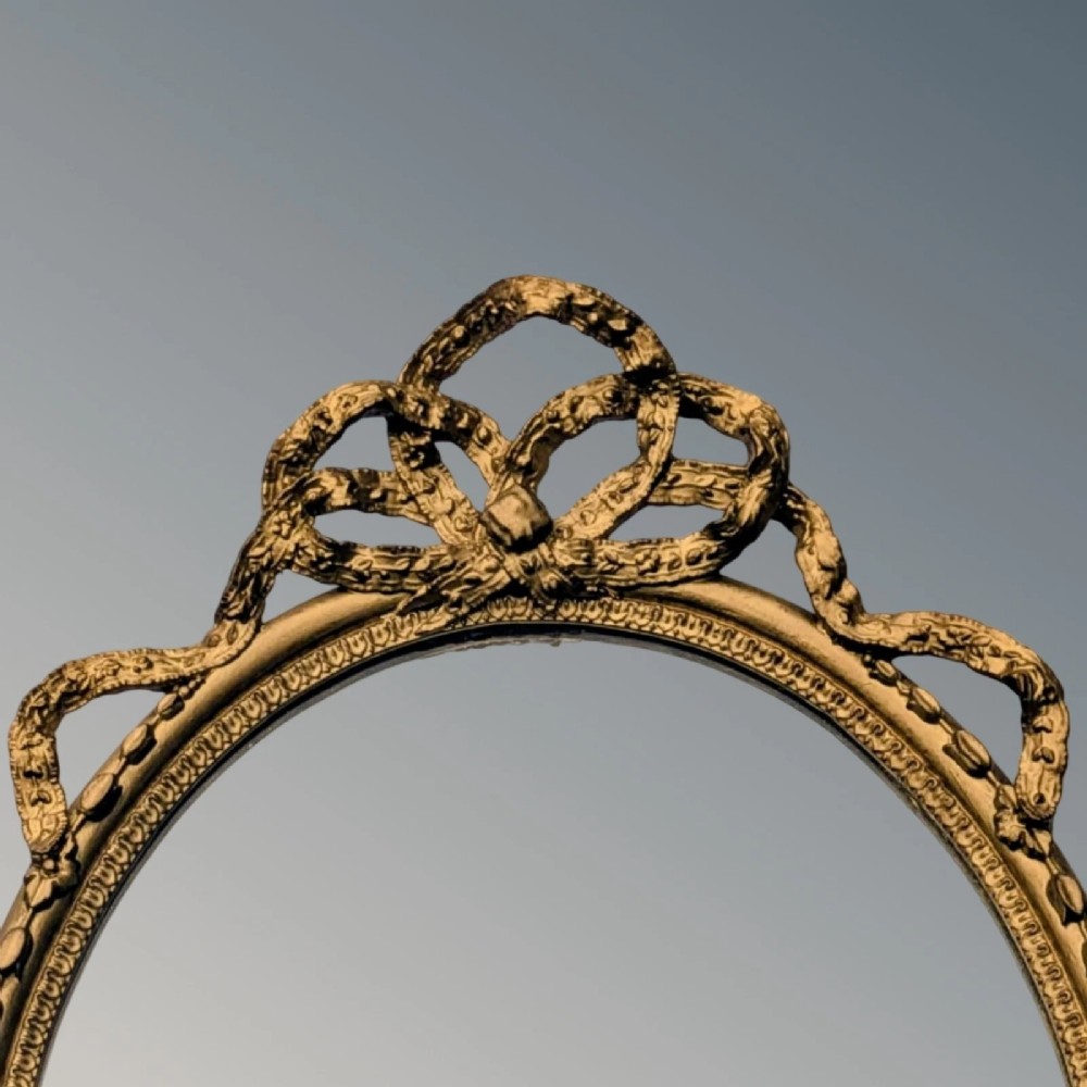 A matching pair of oval giltwood girandole wall mirrors featuring ribbon cresting and twin candle sconces at the base. View VII