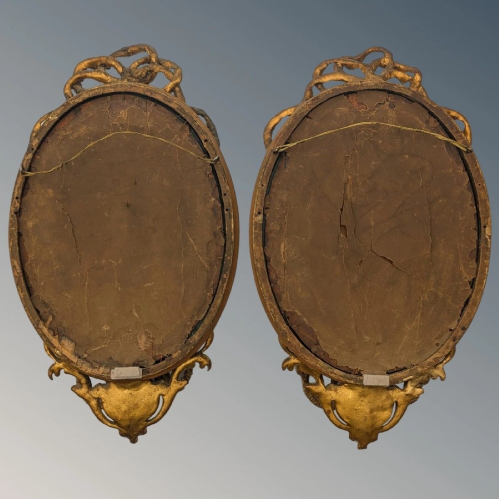 A matching pair of oval giltwood girandole wall mirrors featuring ribbon cresting and twin candle sconces at the base. View VIII