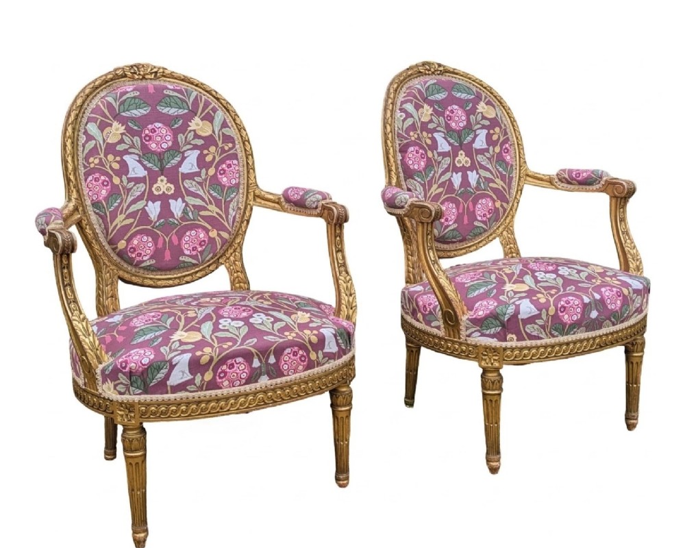 A pair of carved giltwood French armchairs featuring oval medallion backs and floral patterned plum-coloured upholstery.