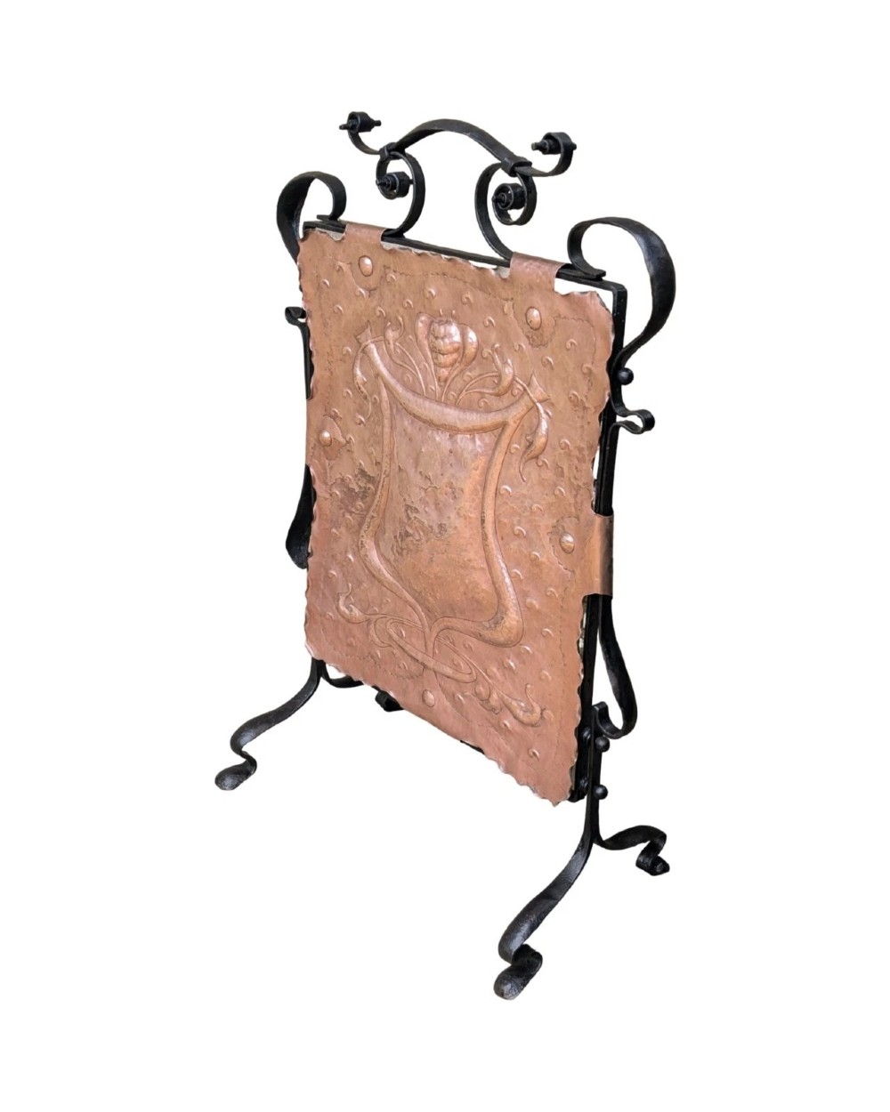 An Arts and Crafts fire screen constructed from a hand-hammered copper central panel with raised relief decoration, held within a black wrought iron scrollwork frame. View II