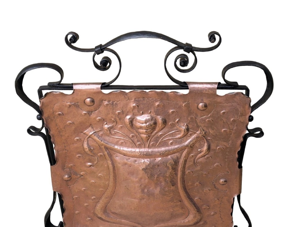 An Arts and Crafts fire screen constructed from a hand-hammered copper central panel with raised relief decoration, held within a black wrought iron scrollwork frame. View III
