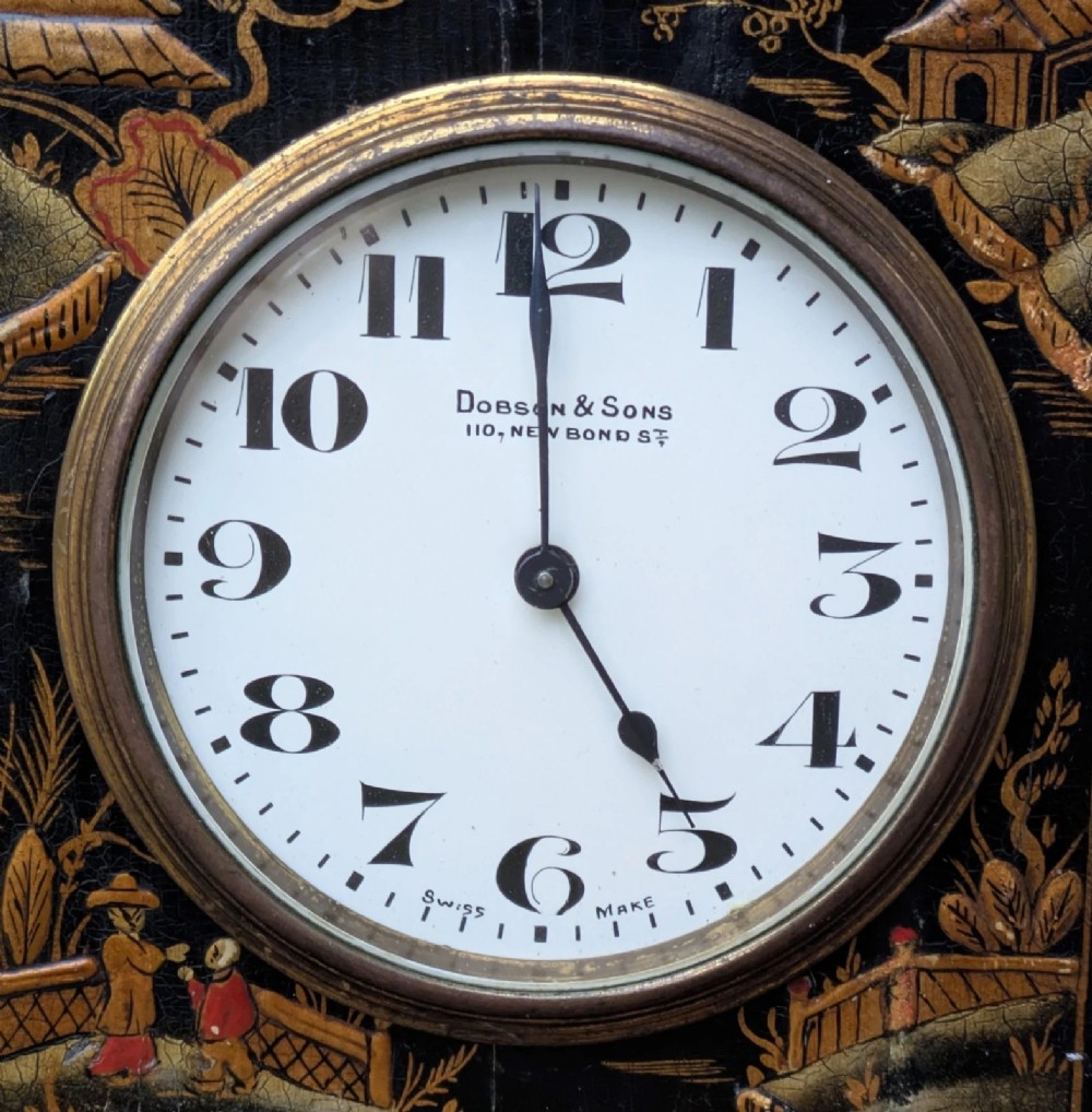 A black lacquered Regency style mantel clock decorated with gold hand-painted Chinoiserie landscapes, featuring a white circular dial with Arabic numerals and a top brass handle. View V
