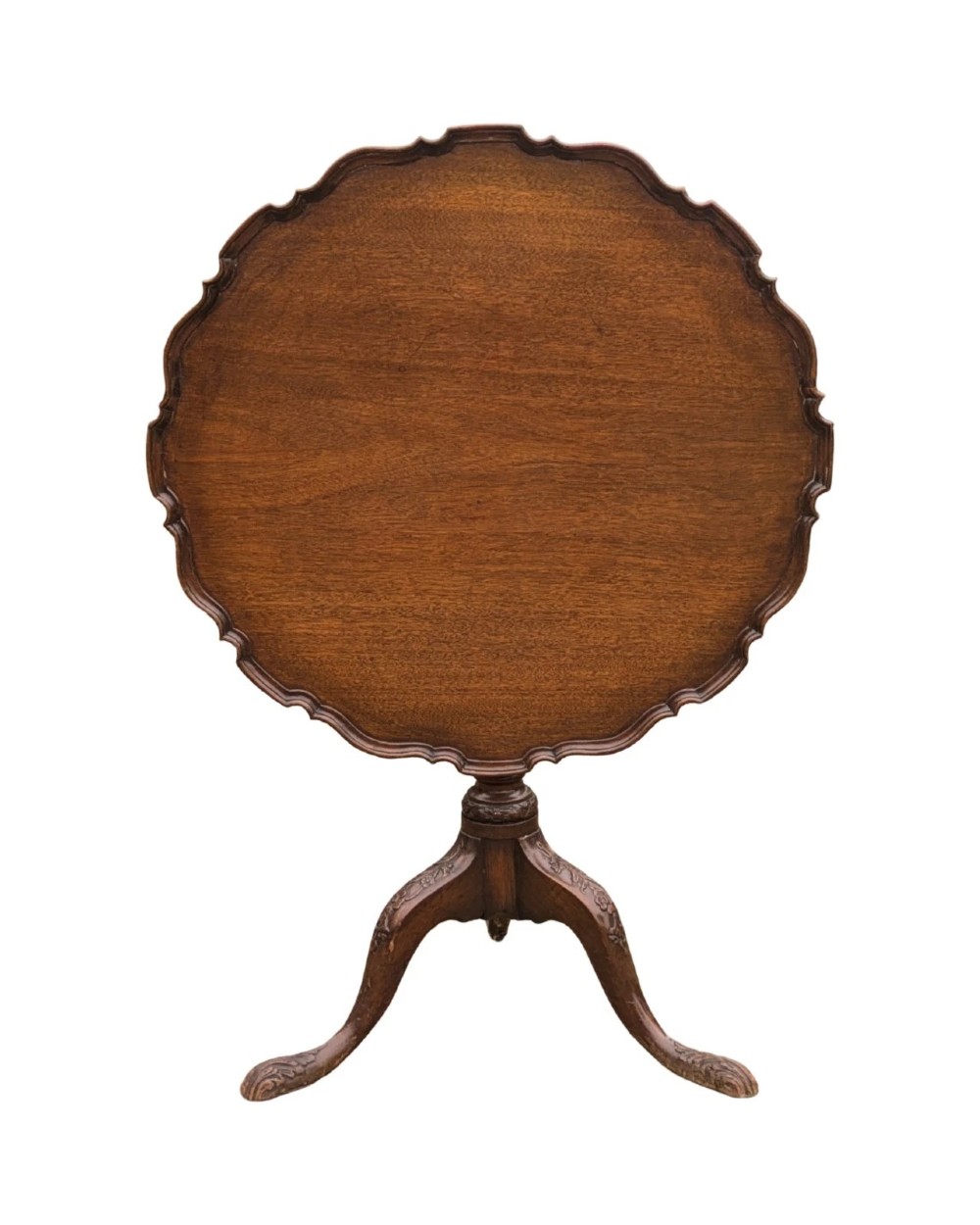 A Georgian mahogany tilt-top table with a scalloped piecrust edge shown in a raised vertical position above a turned pedestal and carved tripod cabriole legs.