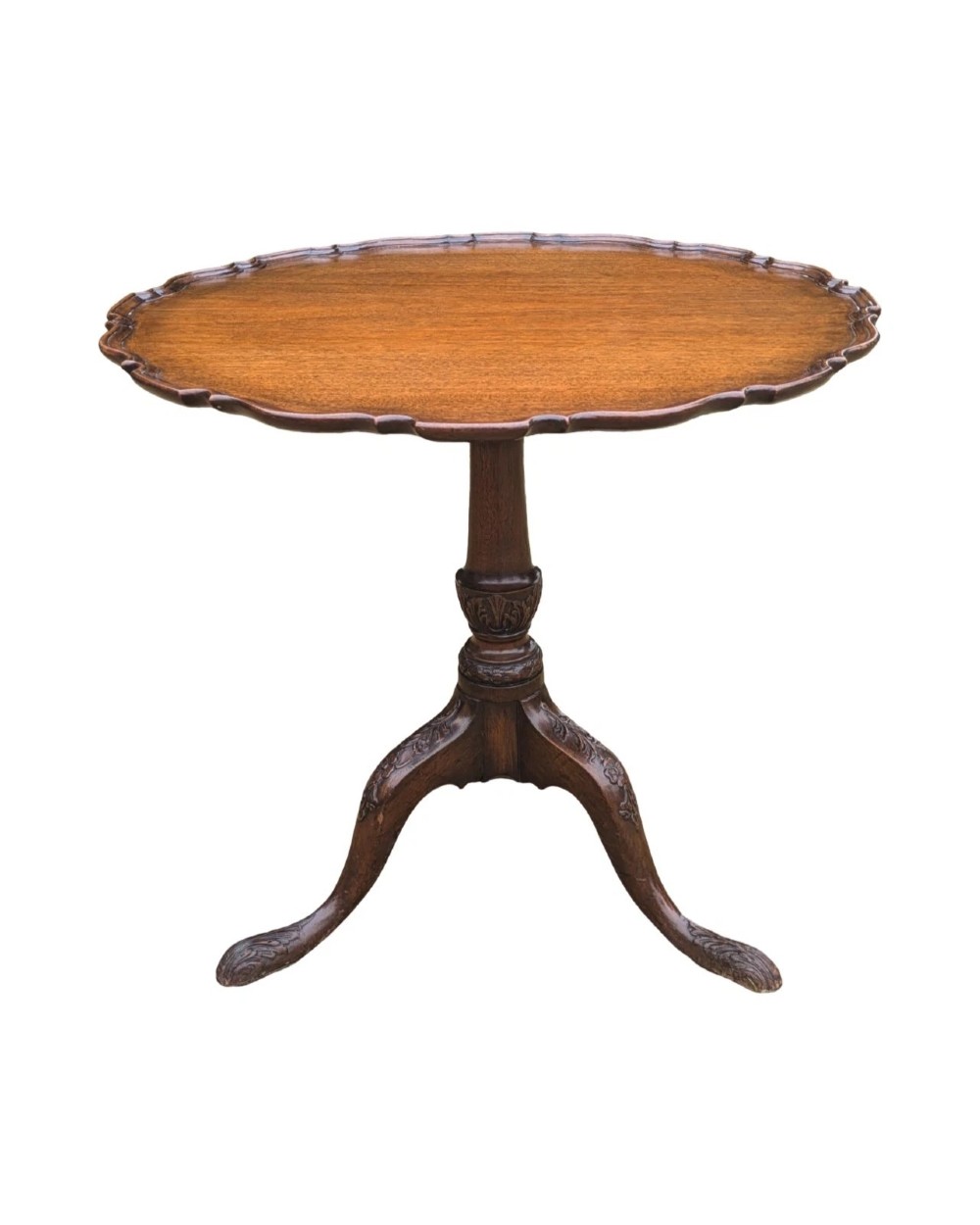 A Georgian mahogany tilt-top table with a scalloped piecrust edge shown in a raised vertical position above a turned pedestal and carved tripod cabriole legs. View II
