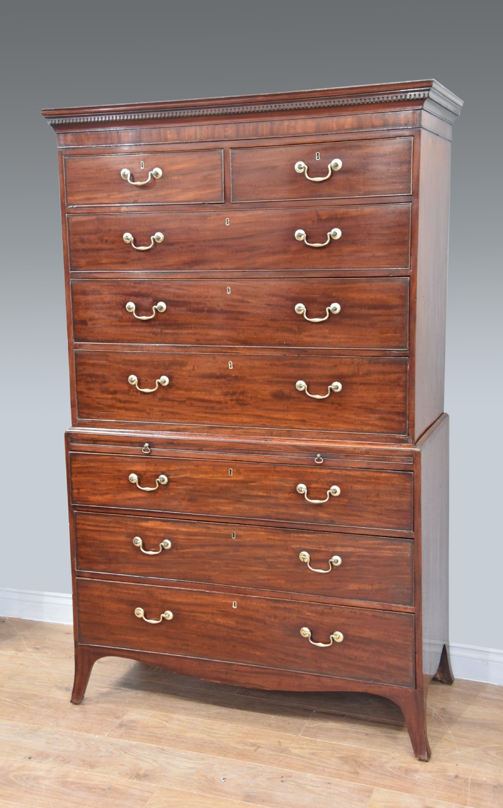 A Georgian mahogany chest on chest featuring two stacked drawer sections, brass swan-neck handles, a dentil cornice, and splayed bracket feet.