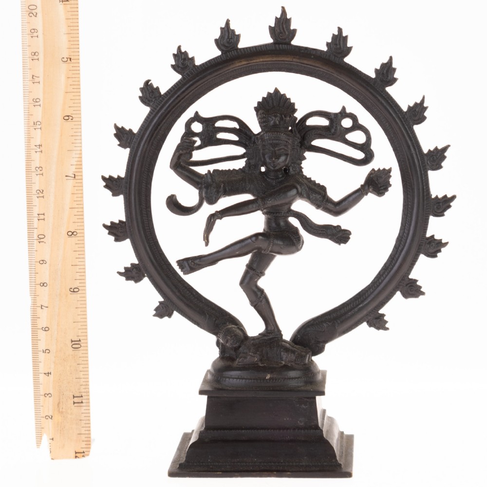 A dark patinated bronze sculpture depicting the Hindu deity Shiva Nataraja as the cosmic dancer encircled by a flaming halo atop a tiered square pedestal. View IV