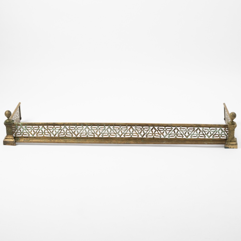 An antique Art Nouveau brass fireplace fender with a pierced floral pattern band and corner finials.
