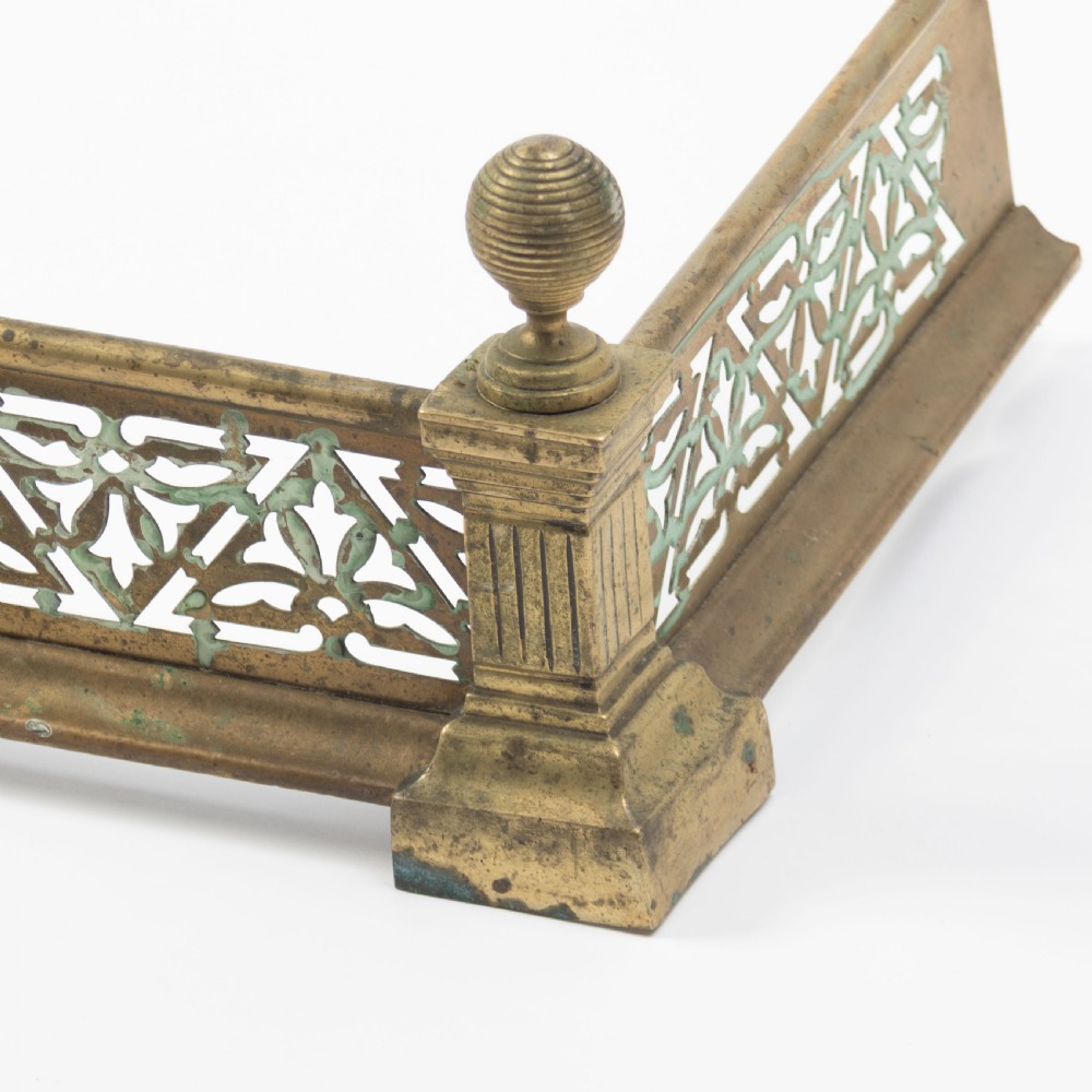 An antique Art Nouveau brass fireplace fender with a pierced floral pattern band and corner finials. View II