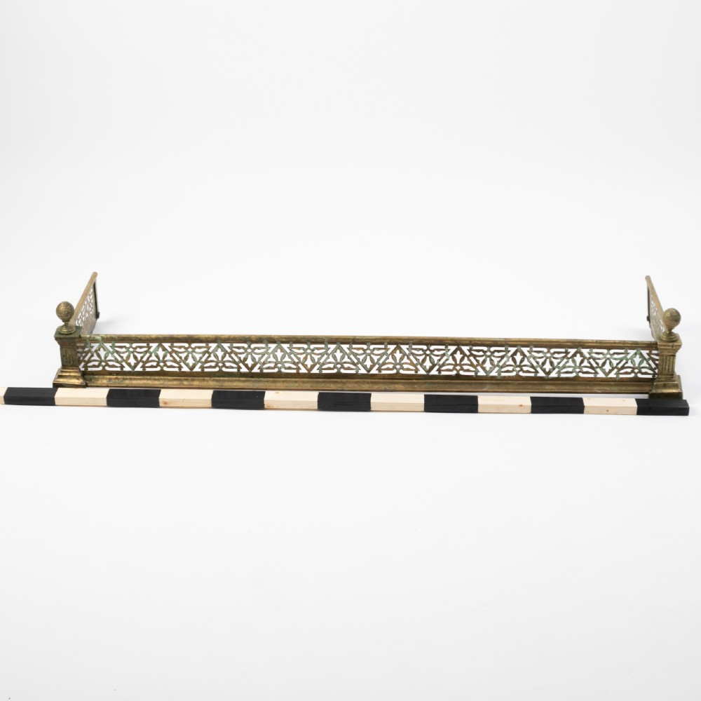 An antique Art Nouveau brass fireplace fender with a pierced floral pattern band and corner finials. View III