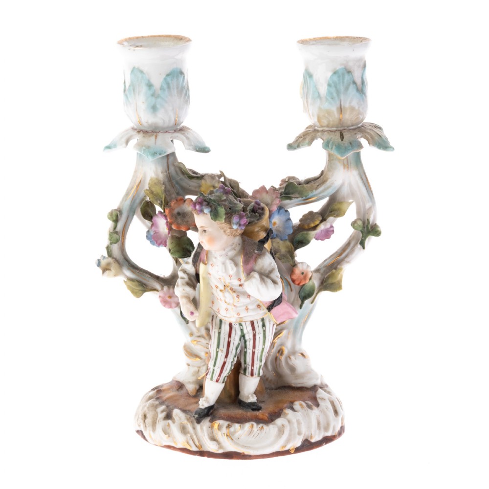 A Dresden porcelain two-light figural candelabrum featuring a youth surrounded by encrusted floral displays and gilt-accented Rococo branch sconces.