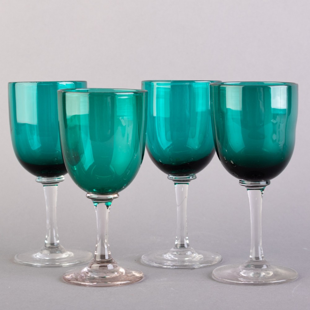 A set of four Victorian Bristol green glass wine goblets featuring clear stems and plain circular bases.