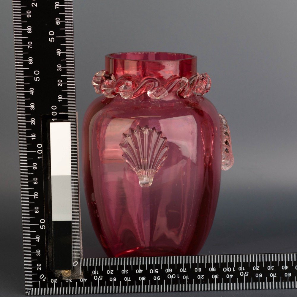A Victorian hand-blown cranberry glass vase featuring an applied clear glass shell motif on the front and a crimped clear glass collar around the neck. View VI