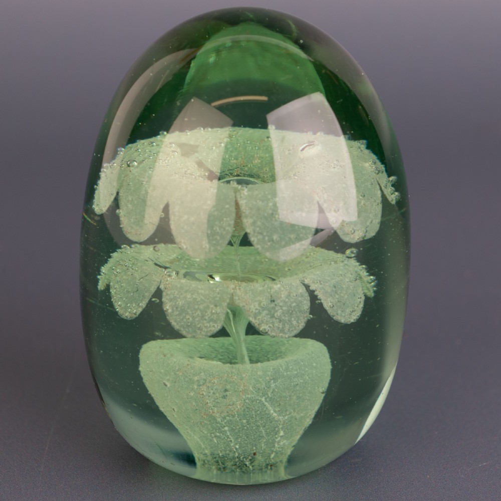 An ovoid green glass dump paperweight featuring trapped air bubble floral patterns inside a solid body.