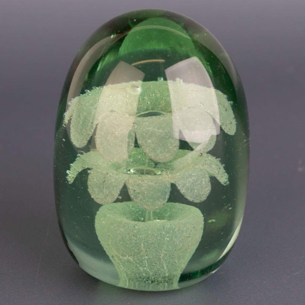 An ovoid green glass dump paperweight featuring trapped air bubble floral patterns inside a solid body. View II