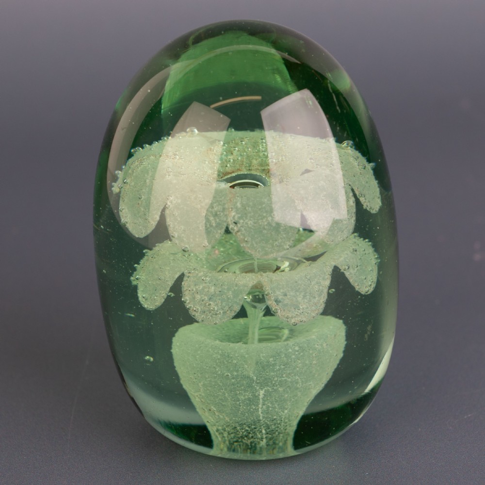 An ovoid green glass dump paperweight featuring trapped air bubble floral patterns inside a solid body. View IV