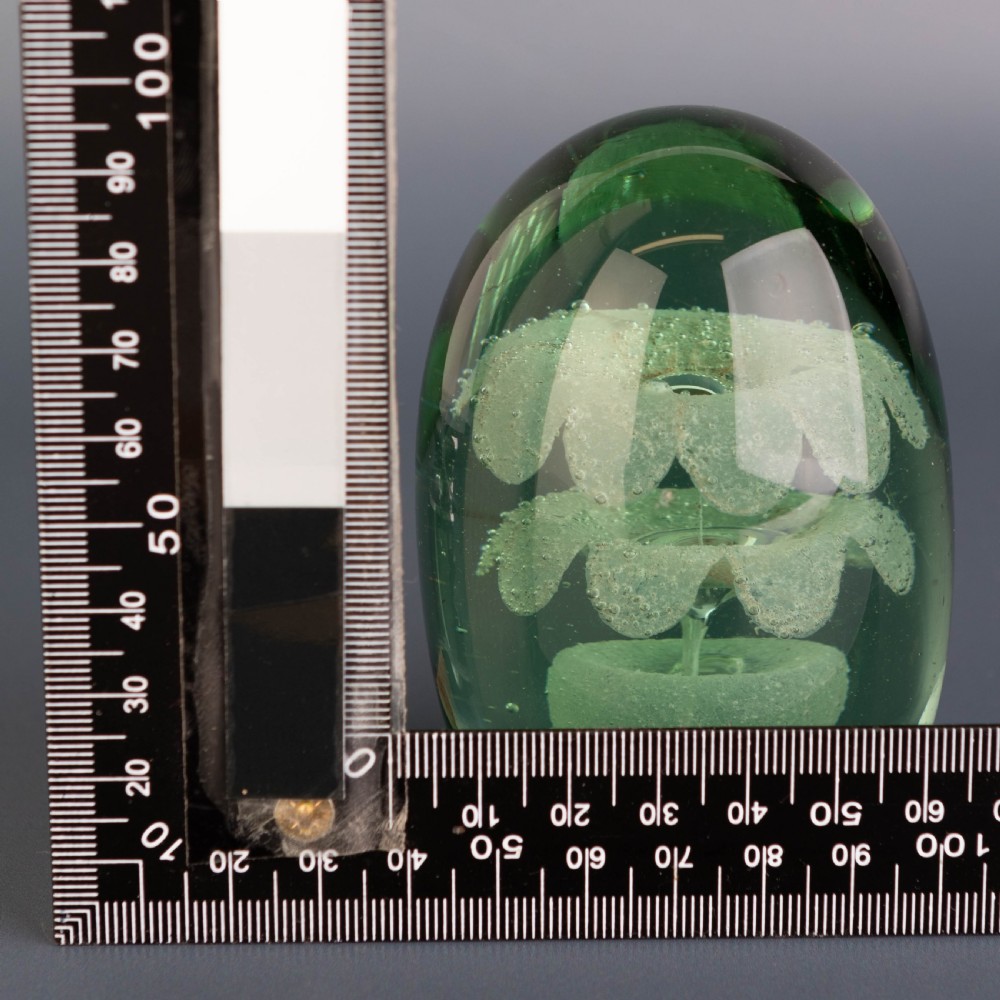 An ovoid green glass dump paperweight featuring trapped air bubble floral patterns inside a solid body. View VI