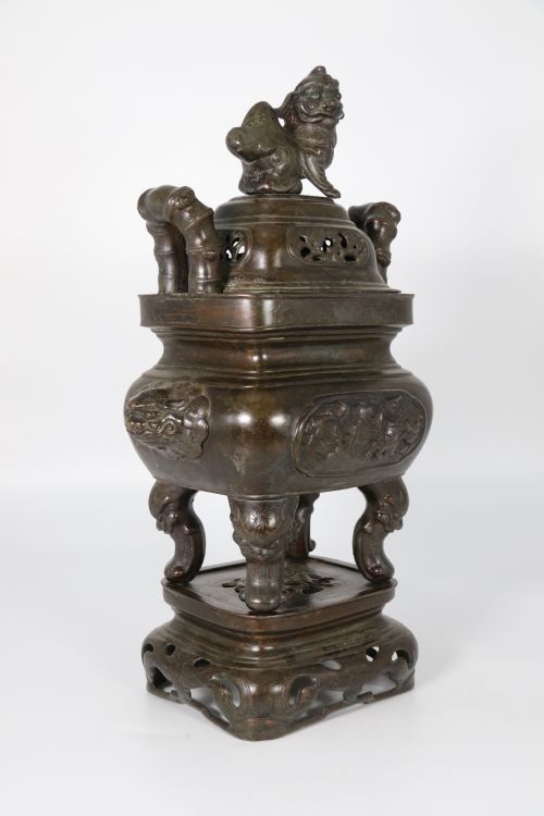 fig 1. A 19th-century Chinese cast bronze incense censer featuring a lid surmounted by a guardian lion finial, relief panels, and animal-mask handles, set upon a matching bronze base.