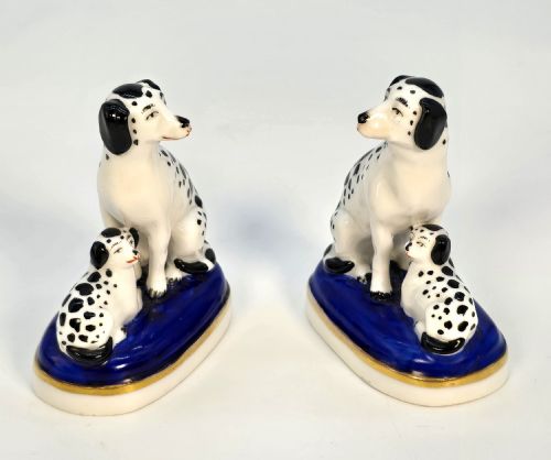 fig 1. A pair of antique porcelain figurines depicting seated black-and-white spotted Dalmatian dogs with puppies on cobalt blue bases with gilt trim.