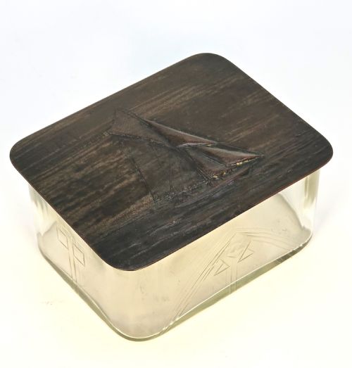 fig 2. A clear glass rectangular box with a patinated bronze lid featuring a raised relief depiction of a sailing boat.
