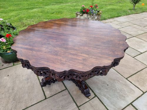 fig 2. A 19th-century Anglo-Indian carved padauk wood centre table featuring a scalloped top, deeply carved pierced apron of foliage, and a pedestal base supported by carved mythical lion feet with brass castors.