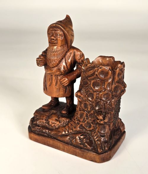 fig 1. A carved limewood match holder depicting a hooded bearded gnome holding a staff beside a hollowed tree stump.