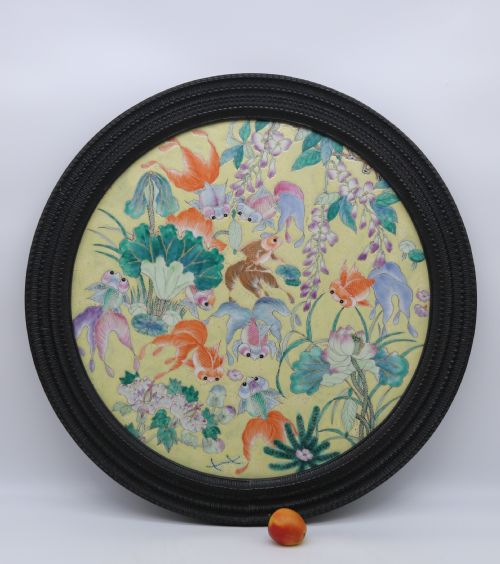 fig 1. A circular framed Chinese porcelain plaque featuring vibrant hand-painted goldfish and lotus flowers on a yellow background enclosed in a carved dark frame.