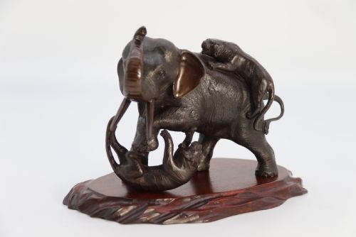 fig 1. A dark patinated bronze sculpture depicting an elephant defending itself against two attacking tigers, mounted on a contoured wooden base.