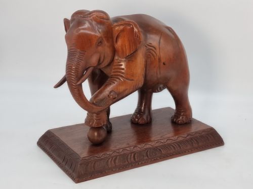 fig 1. A pair of hand-carved warm brown teak wooden elephant sculptures balancing on balls mounted on rectangular bases.