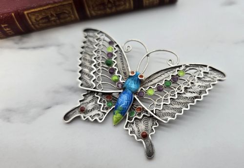 fig 2. A silver filigree butterfly brooch featuring openwork wings filled with blue, green, purple, and red enamel details.