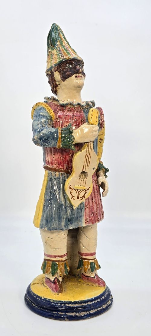 fig 1. A polychrome glazed earthenware figure of a masked Commedia dellArte Pulcinella holding a stringed instrument.