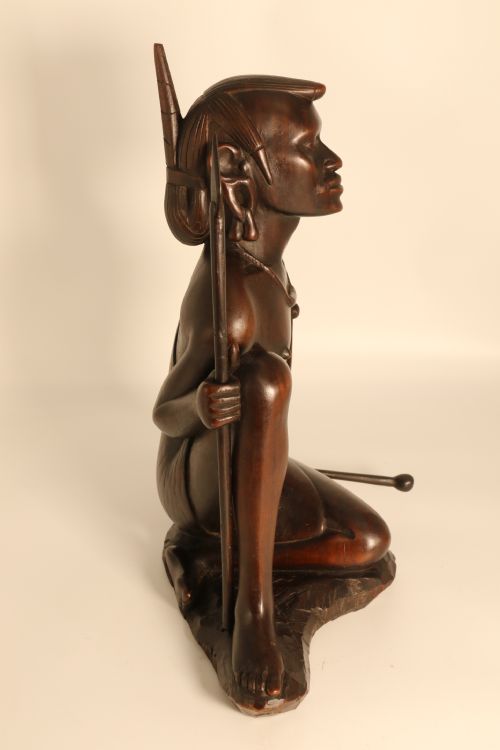 fig 1. A dark hardwood hand-carved sculpture of a kneeling Maasai warrior holding a spear and club on an integrated wooden base.