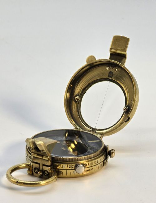 fig 2. An antique Edwardian brass pocket compass with an open hinged lid featuring a glass window, an engraved internal dial, and an attached thumb ring.
